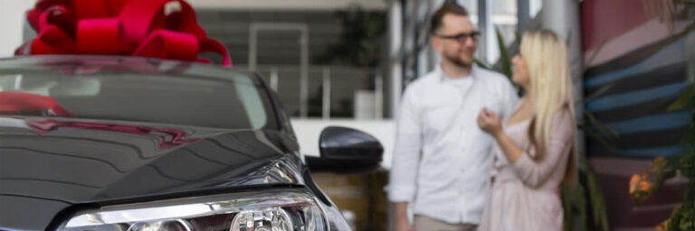 Pół nowego samochodu z czerwoną kokardą i rozmyta para w tle